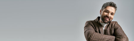 A bearded man in a brown jacket confidently posing in a studio setting against a grey backdrop.の写真素材