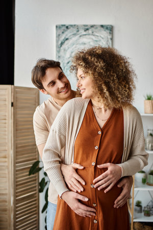 Happy and young pregnant couple, expecting baby couple, man hugging his pregnant wife from behind