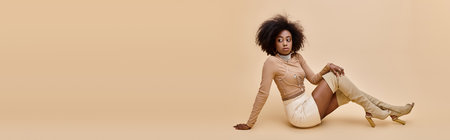 african american girl in trendy outfit and thigh-high boots reclines on beige backdrop, bannerの写真素材