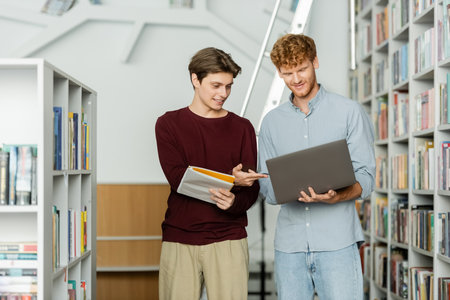 Two men in a library, engrossed in a laptop screen.