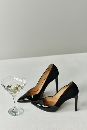 Two black high heels and a martini glass on a white surface.の写真素材