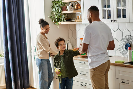 An African American man and woman clean with a child in a cozy kitchen.の写真素材