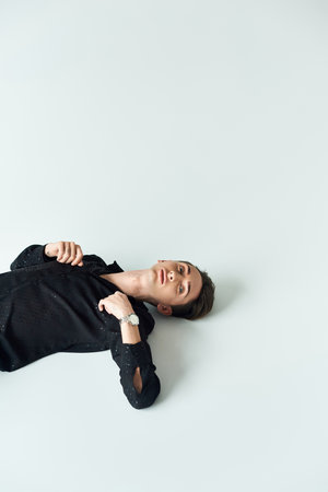 A young queer person lies on his stomach, exuding tranquility and introspection, against a stark...