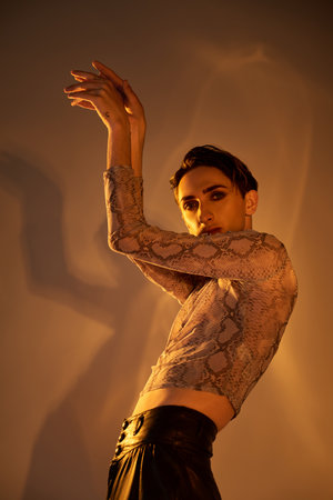 A stylishly dressed young queer person poses with arms outstretched in a show of confidence and...