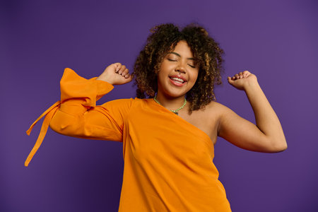 Stylish African American woman striking a pose in an orange dress against a vibrant backdrop.の写真素材