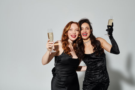 Two elegant women in black dresses joyfully toast with champagne flutes.の写真素材