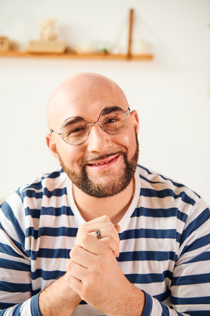 A bald man in glasses strikes a thoughtful pose at home.の写真素材
