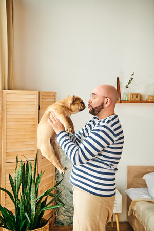 A man lovingly embraces a French bulldog against his face.の写真素材