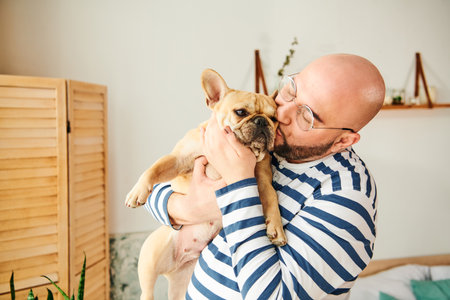 Handsome man with glasses cradling a small French Bulldog in his arms.の写真素材