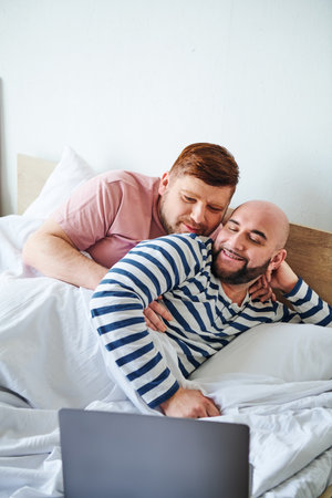 Two men cozy up in bed while using a laptop.の写真素材
