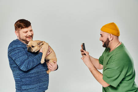 Two men stand closely, holding a French bulldog.