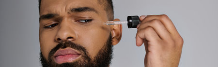 African american stylish man with a beard holding a bottle of serum.の写真素材