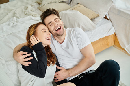 A man and a woman enjoy a peaceful moment, sitting on their bed, deep in conversation, surrounded by...
