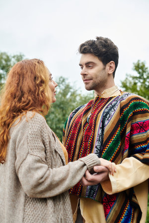 A man and woman, dressed in boho style, stand side by side in a lush green park, exuding a sense of love and connection.の写真素材