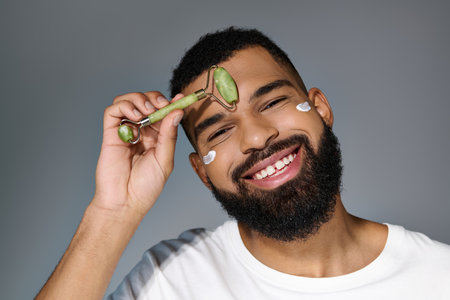 African american bearded man with cream on his face using face roller.の写真素材