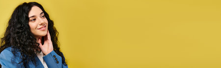 A young, stylish woman with curly hair stands in front of a vibrant yellow wall, showcasing various emotions.の写真素材
