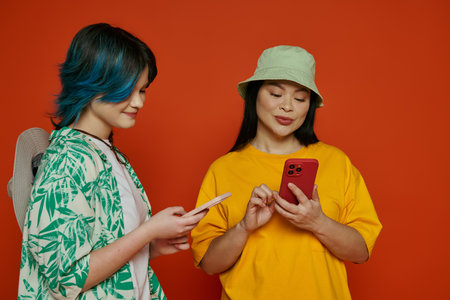 Asian mother and her teenage daughter standing together, engrossed in a cell phone screen, on an...