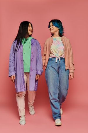 Asian mother and daughter stand side by side against a vibrant pink backdrop in a studio setting.