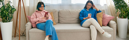 Asian mother and teenage daughter sitting on a couch, sharing a peaceful moment in front of a...