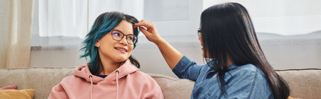 A mother with unique blue hair is tenderly combing her teenage daughters hair at home in a...