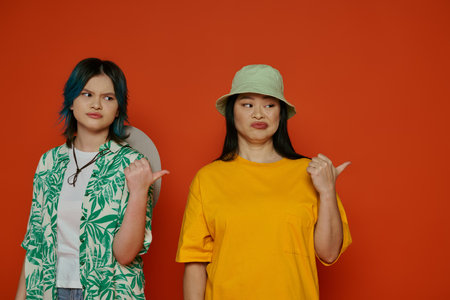Asian mother and her teenage daughter standing together in front of a vibrant red wall.