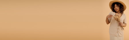 A stunning African American woman with curly hair posing gracefully in a white dress and straw hat in a serene studio setting.の写真素材