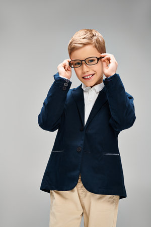 A small, stylishly dressed preadolescent boy wearing glasses strikes a thoughtful pose against a gray backdrop.の写真素材