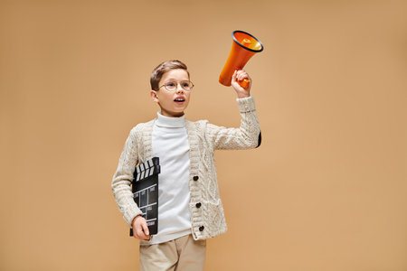 A young boy, dressed as a film director, holds a megaphone and a clapper.