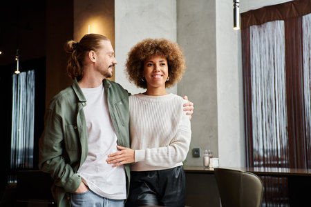 An African American woman and a man stand elegantly together in a modern cafe.の写真素材