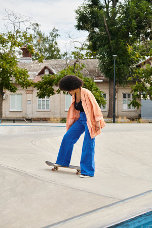 black woman skillfully rides a skateboard on top of a cement ramp in an outdoor skate park.