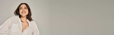 A beautiful plus size woman in a white shirt striking a pose on a gray backdrop.