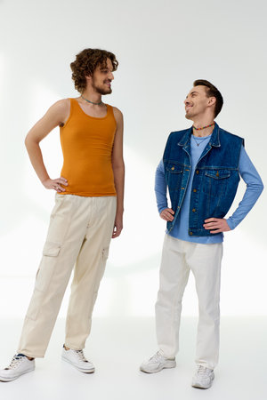 handsome jolly lgbt friends in vivid attires looking at each other on gray backdrop, pride month