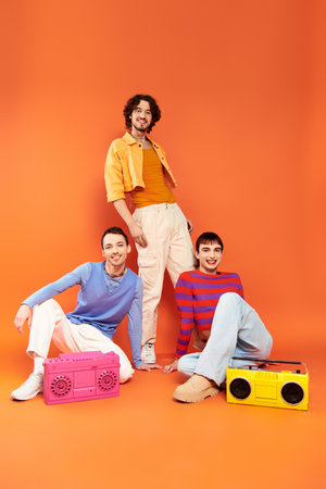 three jolly attractive gay friends in vivid attire posing with tape recorders, pride month