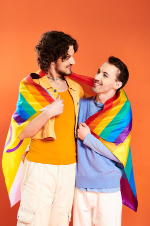joyous appealing young gay men in cozy attires with rainbow flag on orange backdrop, pride monthの写真素材
