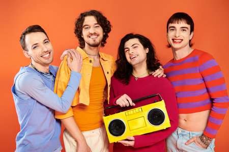 four joyful appealing gay friends posing actively with tape recorder on orange backdrop, pride monthの写真素材