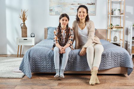 Mother and daughter enjoying quality time, sitting on a bed in a warm room.の写真素材