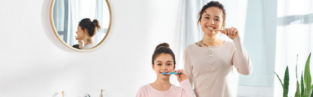 A brunette woman and her preteen daughter engage in their morning routine, brushing their teeth in a modern bathroom.の写真素材