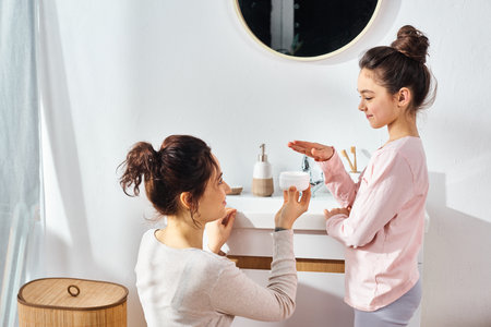A brunette woman and her preteen daughter are standing together in a modern bathroom, engaged in their beauty and hygiene routine.の写真素材