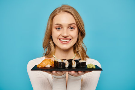 A beautiful blonde woman delicately holds a plate of freshly prepared sushi.の写真素材
