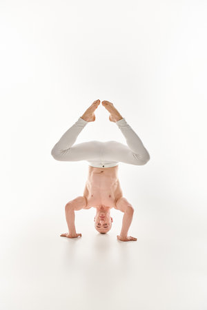 A young man showcases his acrobatic skills by performing a headstand, captured in a studio against a...