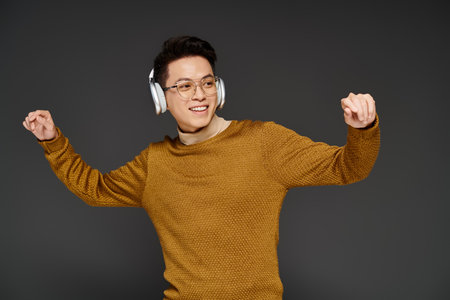 A fashionable young man energetically poses in a cozy sweater while wearing headphones, exuding a trendy and sophisticated vibe.の写真素材