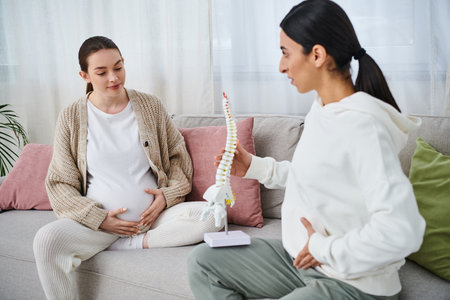 Two women, one pregnant, engage in a deep discussion while seated on a cozy couch during a prenatal course.の写真素材