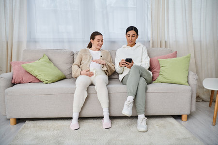 A man and pregnant woman sit on a sofa, engrossed in a cell phone screen, likely sharing a moment of connection.の写真素材