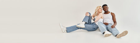 A young interracial couple sitting gracefully on the ground in a studio against a grey background.の写真素材