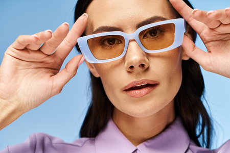 A fashionable woman in a purple shirt and blue sunglasses against a vibrant blue background.