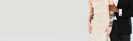 A beautiful blonde bride in a wedding dress and an African American groom standing next to each other in a studio on a grey background.の写真素材