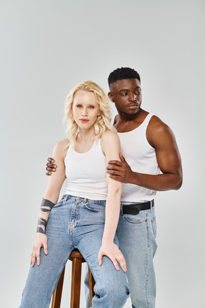 A young interracial couple sitting on a stool in a studio against a grey background.の写真素材