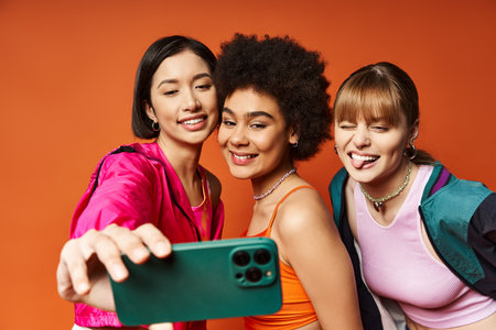 Three diverse women of Caucasian, Asian, and African American descent taking a selfie with a cell...