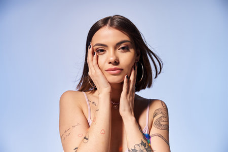 A young woman with brunette hair proudly displays a tattoo on her arm while striking a pose in a studio setting.の写真素材