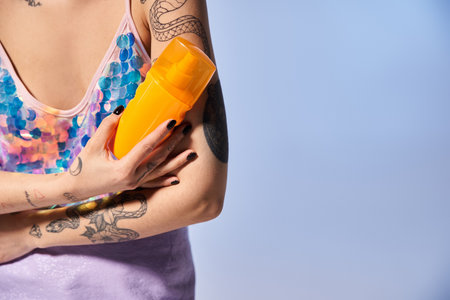 A young woman with tattoos, brunette hair, holding a yellow sunscreen in a studio setting.の写真素材